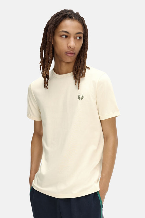T-shirt écru de FRED PERRY avec un logo de couronne de laurier vert, porté par un homme aux dreadlocks et un pantalon bleu marine.