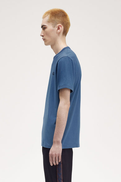 Blauwe korte mouw T-shirt van FRED PERRY, zijkant weergave, met discreet logo en zwarte broek met decoratieve band.