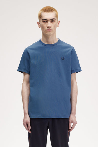 Blauwe korte mouw T-shirt van FRED PERRY, versierd met een gestikte logo op de borst, gedragen met een donkere broant.