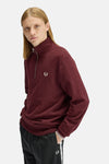 Burgundy half-zip sweatshirt with ribbed cuffs and chest laurel wreath embroidery by Fred Perry, worn in side view with black pants featuring white stripe.