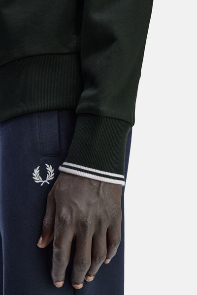 Groene sweater, van FRED PERRY, met geribde manchetten met witte strepen en gedragen met een marineblauwe joggingbroek.