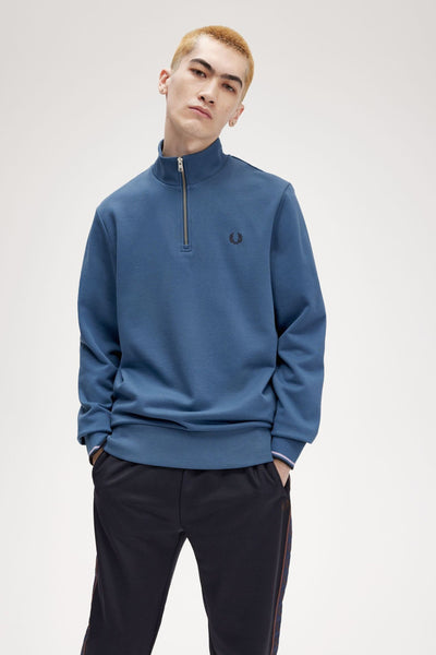 Blauwe sweater met opstaande kraag van FRED PERRY, met ritssluiting en zwarte joggingbroek met strepen.