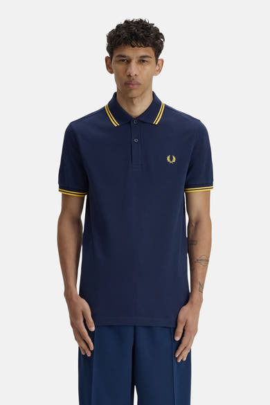 Polo bleu à manches courtes de FRED PERRY, avec rayures jaunes sur le col et les manches, et logo brodé sur la poitrine.