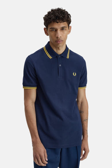 Polo bleu à manches courtes de FRED PERRY, avec col et bords de manches jaunes, logo brodé sur la poitrine.