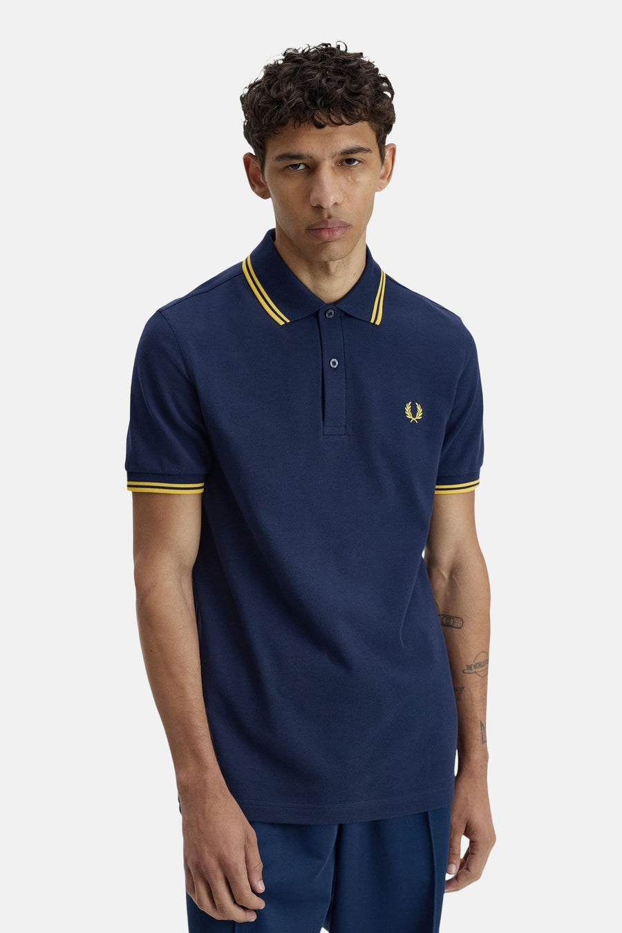 Polo bleu à manches courtes de FRED PERRY, avec col et bords de manches jaunes, logo brodé sur la poitrine.