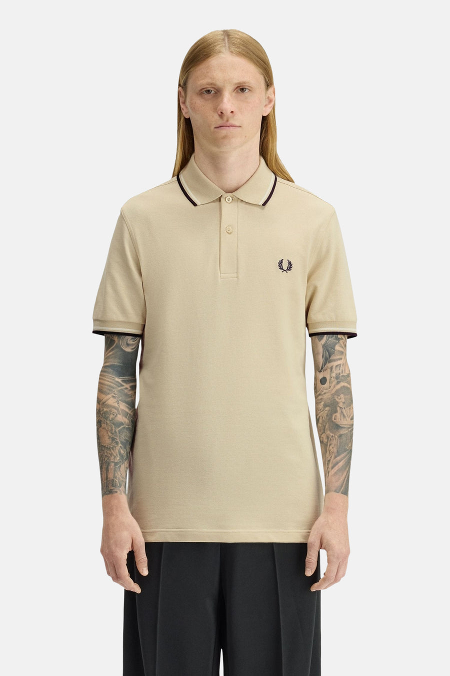 Beige poloshirt met korte mouwen van FRED PERRY, met gestreepte details op de kraag en mouwen, gedragen met een zwarte broek.