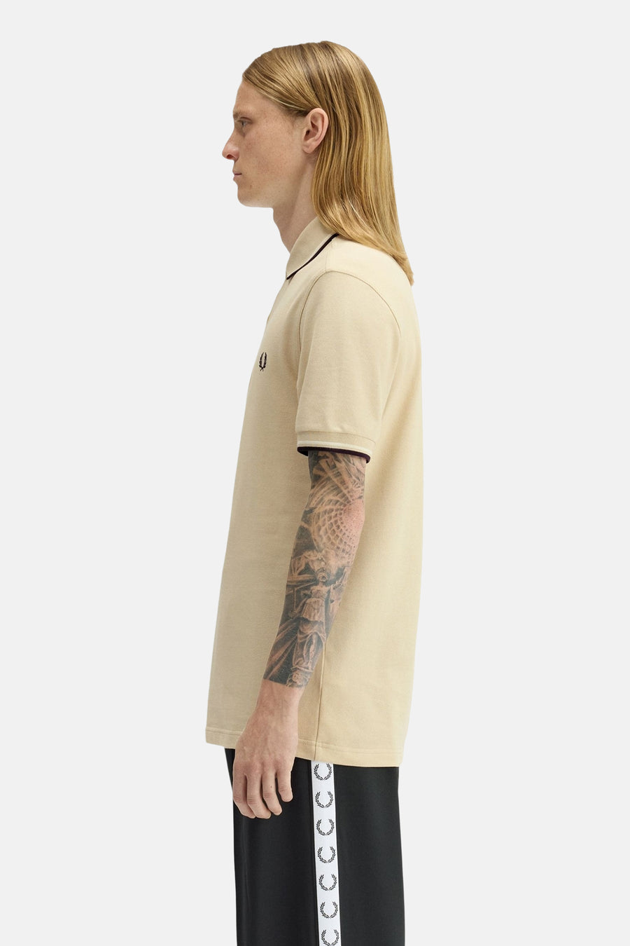 Polo à manches courtes beige de Fred Perry, avec détails de bordure noirs et manches tatouées, en vue latérale.