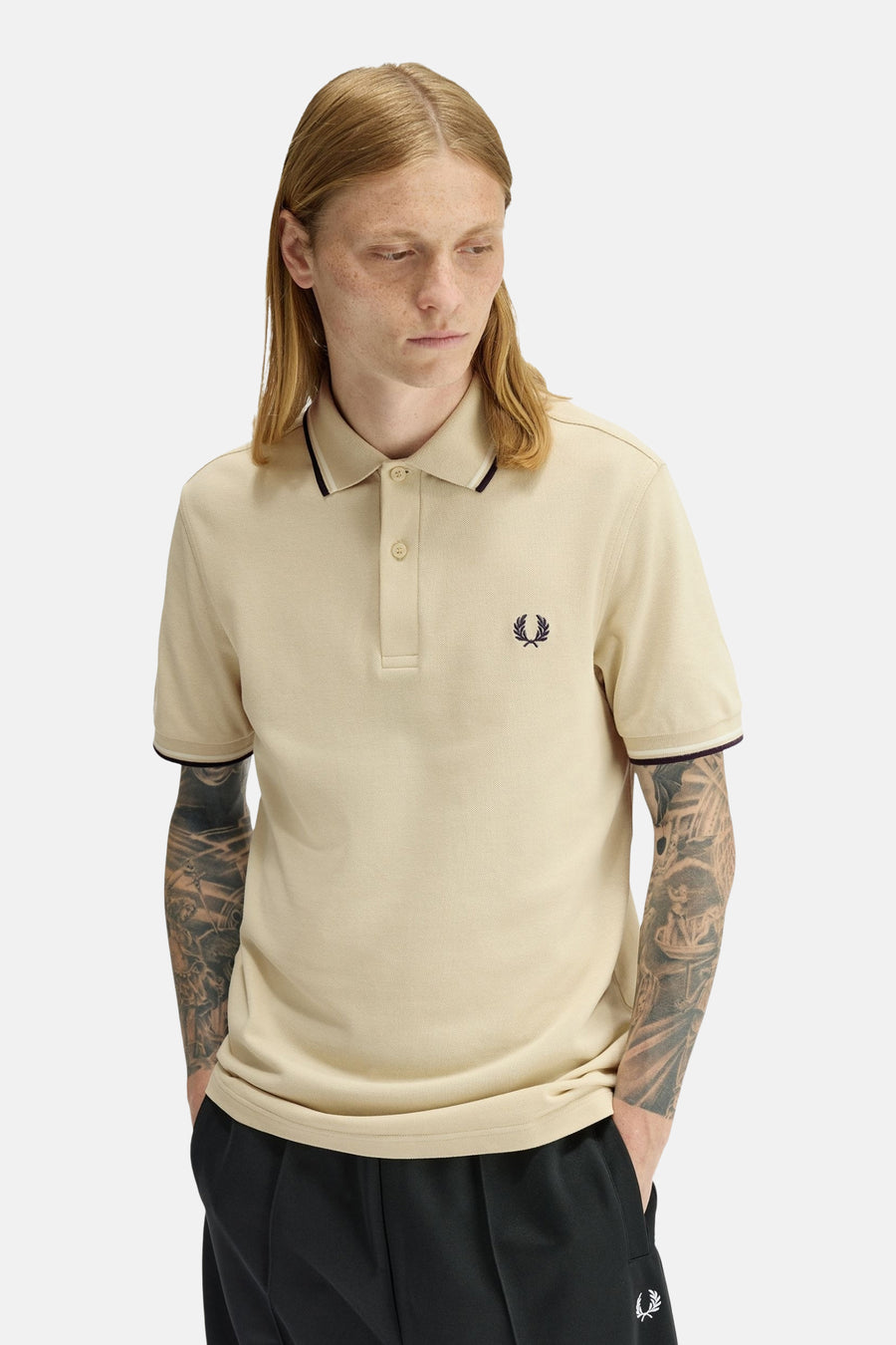 Polo à manches courtes beige de FRED PERRY, avec détails rayés au col et aux manches, porté avec un pantalon noir.