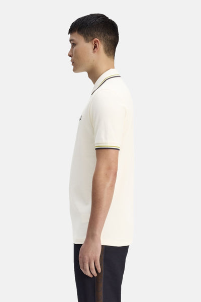 Ecru polo van FRED PERRY met contrasterende strepen op de kraag en korte mouwen, gedragen met een zwarte broek.