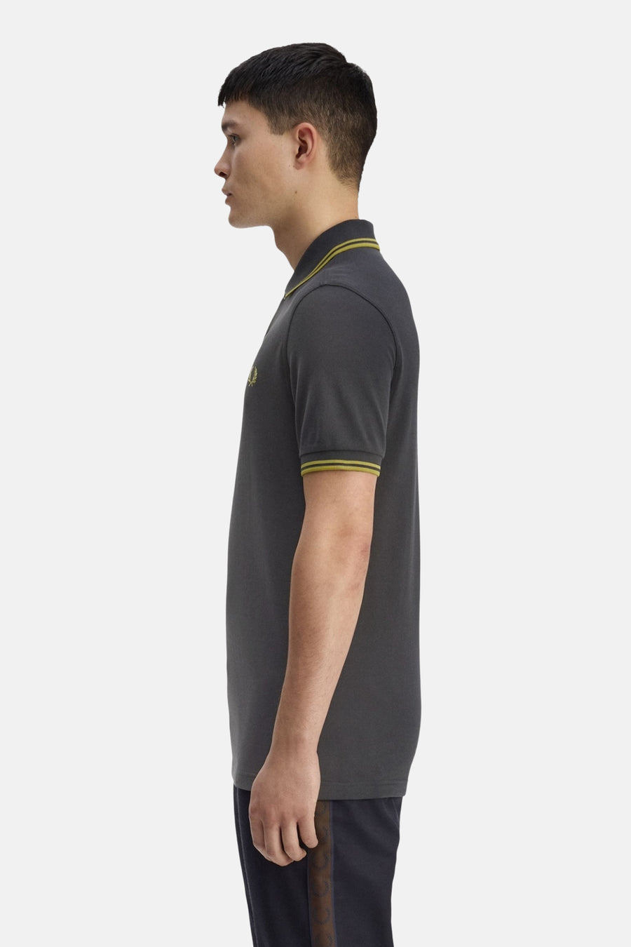 Grijs gemêleerd poloshirt van FRED PERRY, met gele bies op de kraag en mouwen, gedragen met een donkerblauwe broek.