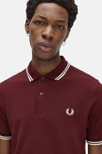 Polo bordeaux à manches courtes de Fred Perry, avec rayures blanches au col et logo sur la poitrine.