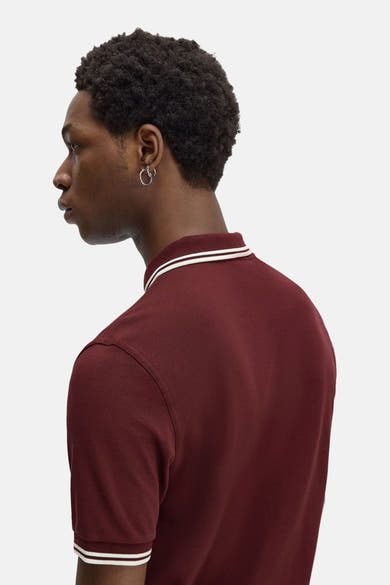 Polo bordeaux à manches courtes de Fred Perry, avec rayures blanches au col et aux manches.