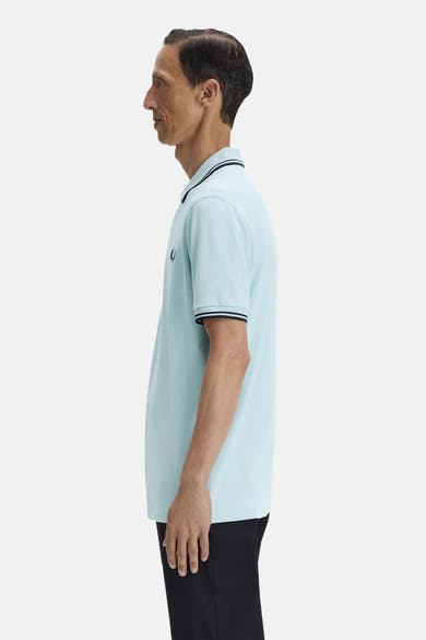 Polo à manches courtes bleu, par FRED PERRY, avec rayures noires au col et aux manches, vu de côté.
