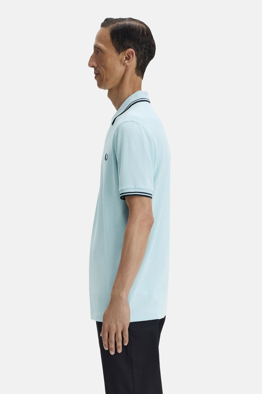 Polo à manches courtes bleu, par FRED PERRY, avec rayures noires au col et aux manches, vu de côté.
