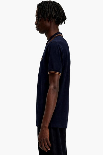 Navy blue polo shirt with gold trim on collar and sleeves, side view of model wearing dark pants.
