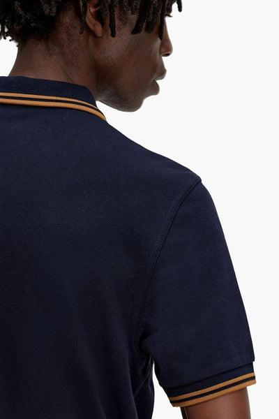 Navy blue polo shirt with orange and black striped collar and cuffs, side view showing textured piqué fabric