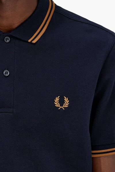 Navy blue pique polo shirt by Fred Perry with gold laurel wreath embroidery and striped collar, close-up front view