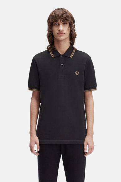 Polo noir à manches courtes de FRED PERRY, avec liserés dorés au col et aux manches, logo doré brodé.
