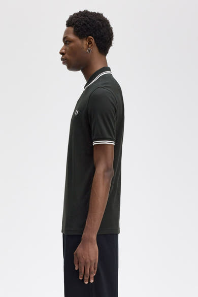 Polo vert par FRED PERRY, coupe classique, liseré blanc au col et aux manches courtes, porté avec un pantalon noir uni.