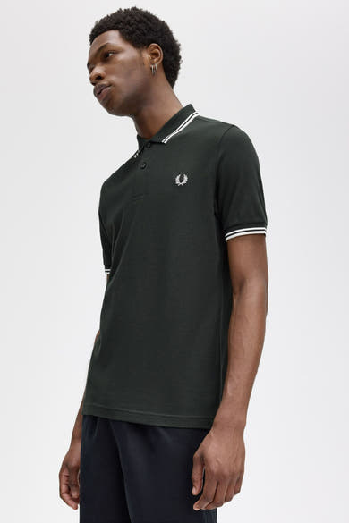 Polo vert de FRED PERRY avec rayures blanches au col et manches, porté avec un pantalon noir.