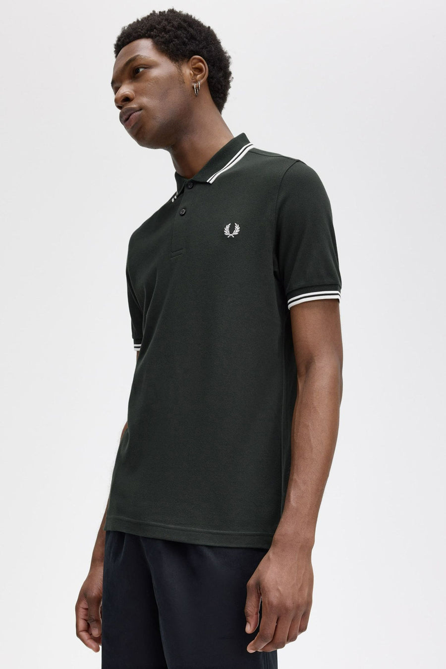 Polo vert de FRED PERRY avec rayures blanches au col et manches, porté avec un pantalon noir.