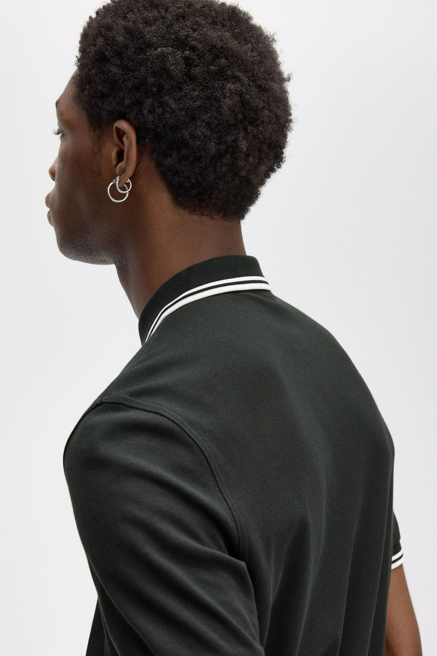 Polo vert de FRED PERRY avec col et bordures blanches, porté avec des boucles d'oreilles argentées.
