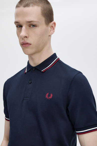 Polo bleu marine à manches courtes de FRED PERRY, avec détails rayés rouge et blanc au col et aux manches.