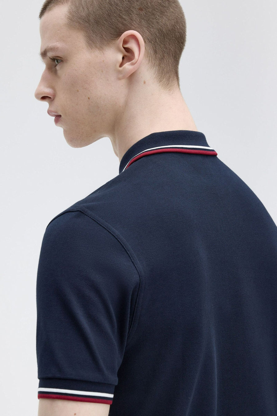 Polo bleu à manches courtes de FRED PERRY, col rayé rouge et blanc, en coton piqué.