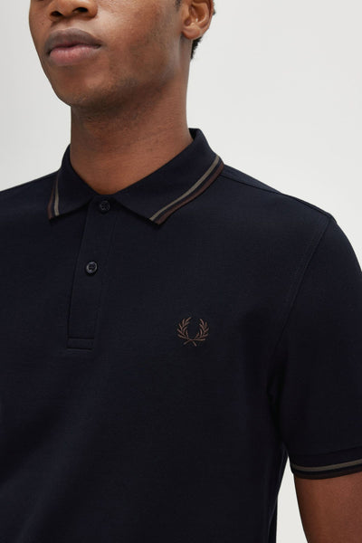 Polo bleu à manches courtes de FRED PERRY, avec rayures contrastantes au col et logo brodé.
