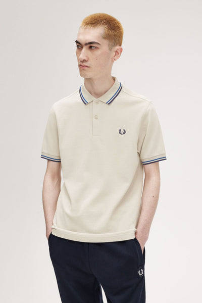 Polo beige par FRED PERRY, détails rayés au col et aux manches, porté avec un pantalon de survêtement bleu marine.