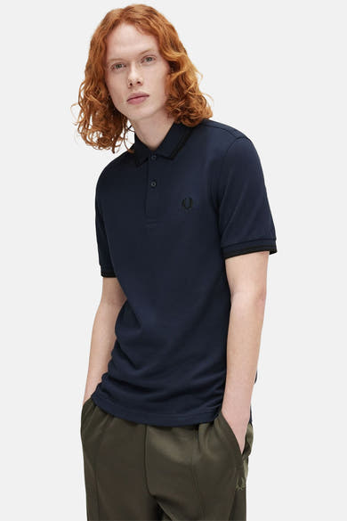 Polo-shirt met FRED PERRY, blauw marine, met een zwarte kragen en mouwen. Dragen met een oliegroene broek.