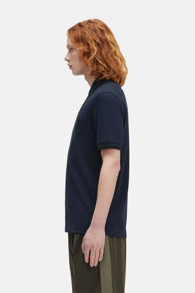Blauwe korte mouw polo van FRED PERRY, gedragen met een khaki broek, zijkant.