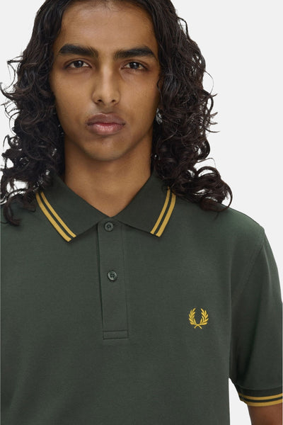 Polo à manches courtes vert de Fred Perry, avec col et manches rayés jaune, logo brodé.
