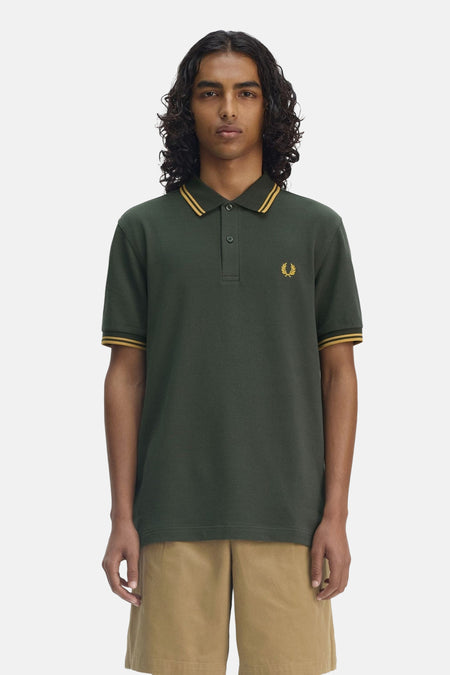 Polo vert à manches courtes de Fred Perry, avec finitions rayées jaunes au col et aux manches, et logo brodé.