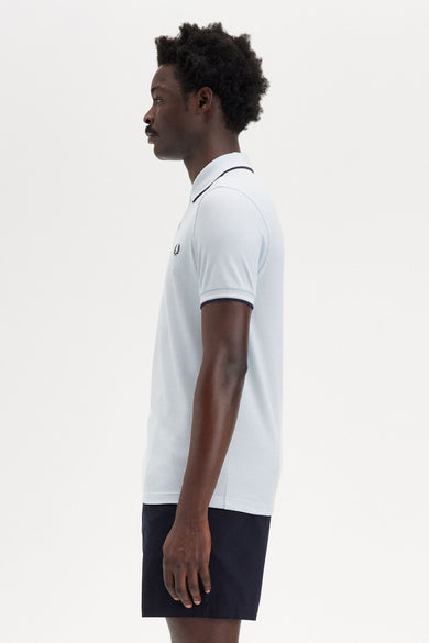 Polo bleu à manches courtes de Fred Perry, avec garniture contrastée au col et aux manches, porté avec un short foncé.