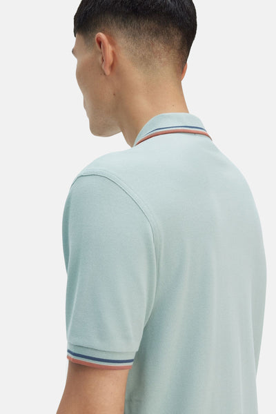 Polo bleu à manches courtes de Fred Perry, avec bordures rayées au col et aux manches.
