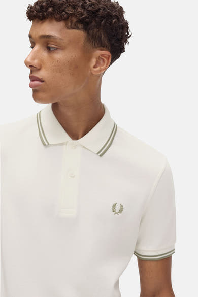 Polo écru à manches courtes de Fred Perry, avec double liseré vert olive au col et aux manches.