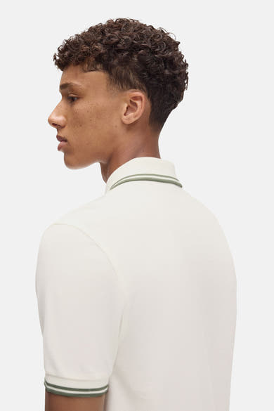Polo écru à manches courtes de Fred Perry, avec rayures vertes au col et aux manches.