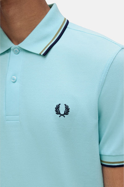 Polo turquoise à manches courtes de Fred Perry, avec détails rayés au col et logo brodé.

