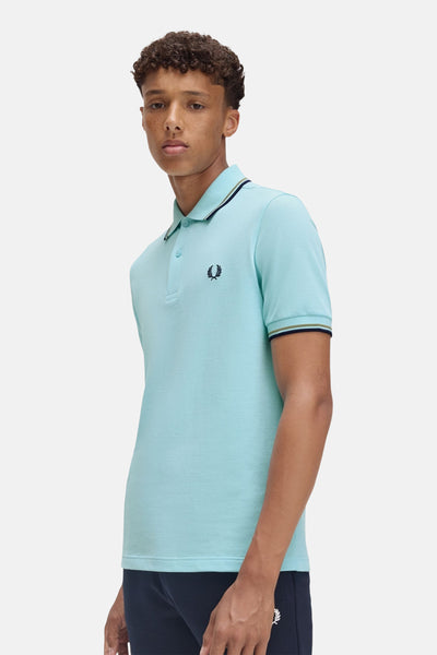 Polo turquoise à manches courtes de Fred Perry, avec liserés contrastants au col et aux manches.