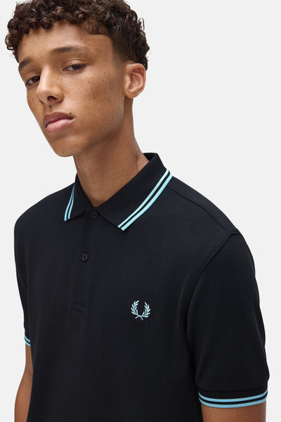 Polo à manches courtes bleu foncé de Fred Perry, avec rayures bleu clair au col et aux manches.