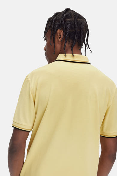 Polo jaune à manches courtes de FRED PERRY, avec bordures noires et dorées au col et aux manches.