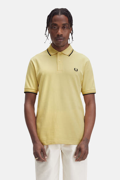 Polo à manches courtes jaune de Fred Perry, avec bordures noires au col et aux manches, et logo brodé.