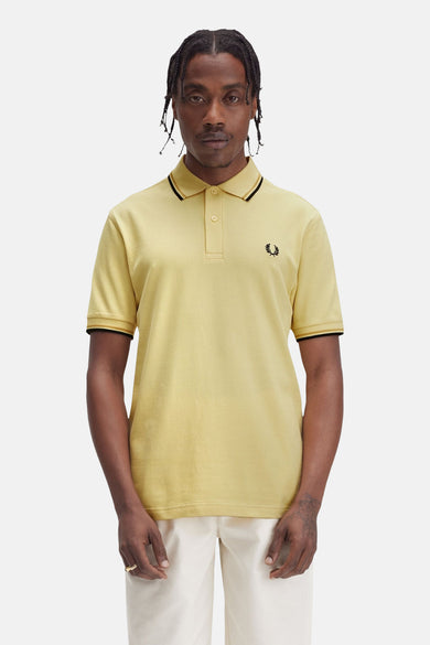 Gele poloshirt met korte mouwen van Fred Perry, met zwarte randen aan de kraag en mouwen, en geborduurd logo.