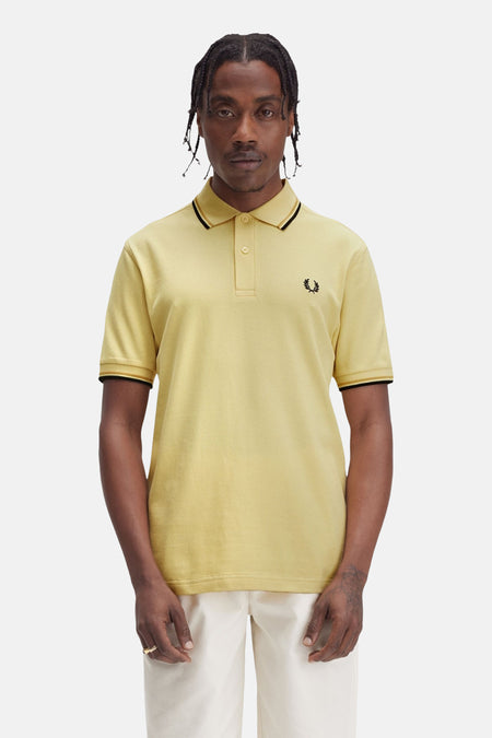 Gele poloshirt met korte mouwen van Fred Perry, met zwarte randen aan de kraag en mouwen, en geborduurd logo.