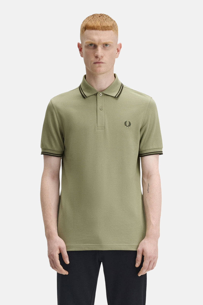 Polo à manches courtes olive de Fred Perry, avec col et manches à rayures noires et logo brodé.
