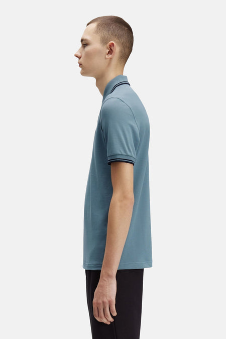 Blauwe polo met korte mouwen van FRED PERRY, met gestreepte afwerkingen aan de kraag en mouwen.