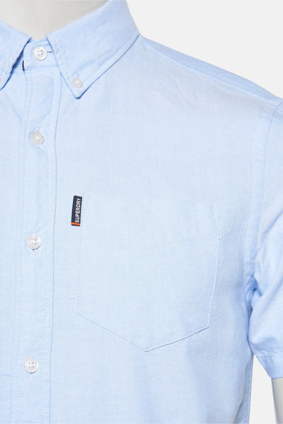Chemise bleue à manches courtes de SUPERDRY, avec poche poitrine et logo discret sur le côté.