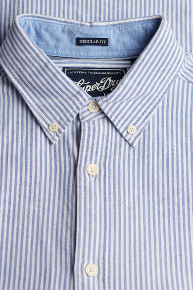 Chemise à manches longues bleue à rayures, de SUPERDRY, avec col boutonné et détails de l'étiquette.