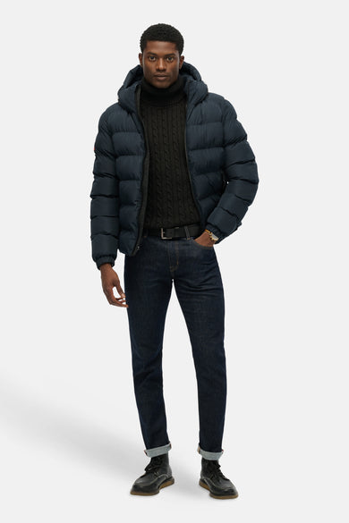 Veste courte bleue de SUPERDRY, portée avec un pull à col roulé en maille torsadée et un jean sombre.
